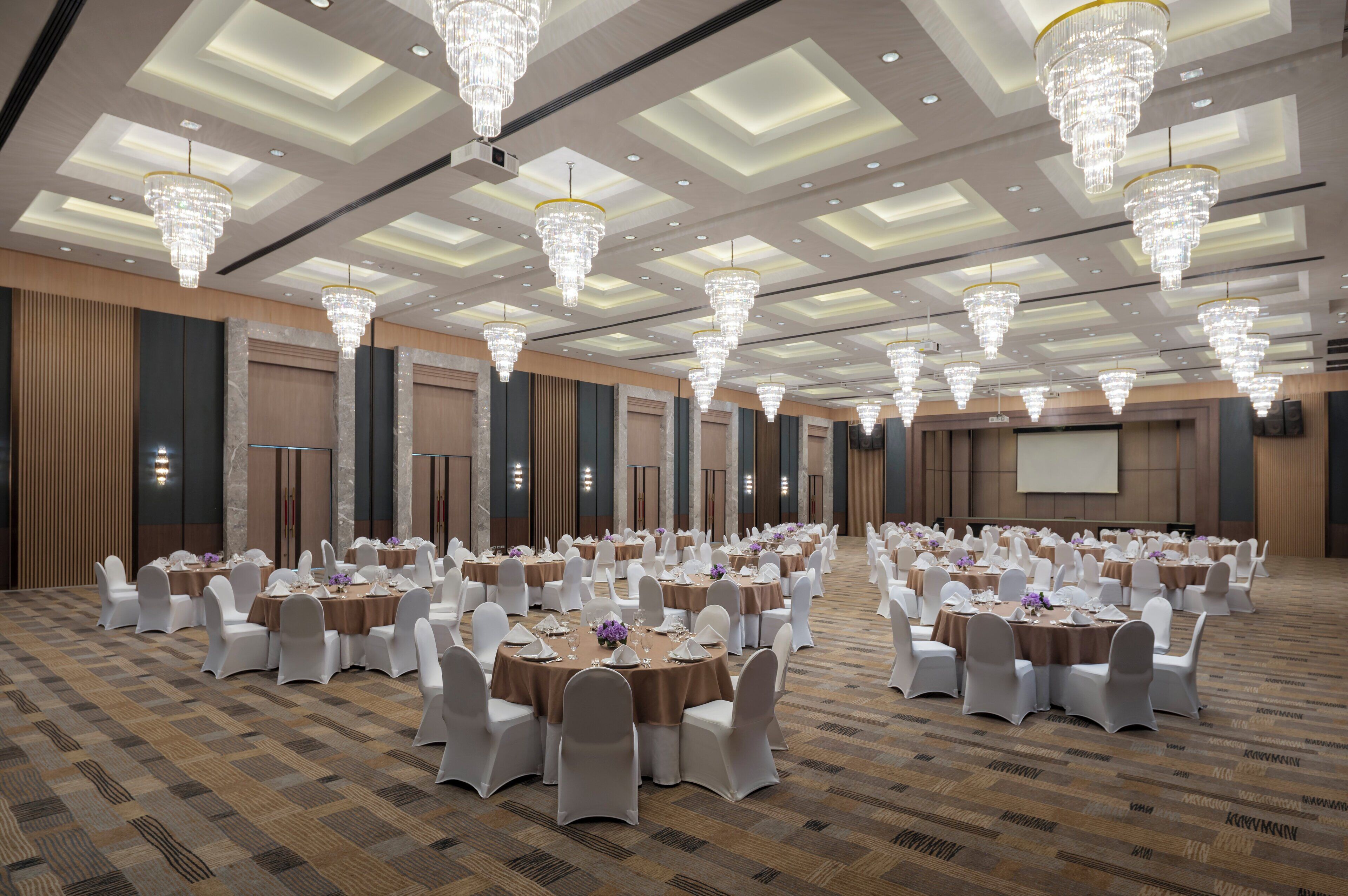 A large banquet hall with round tables, white chairs, and chandeliers.