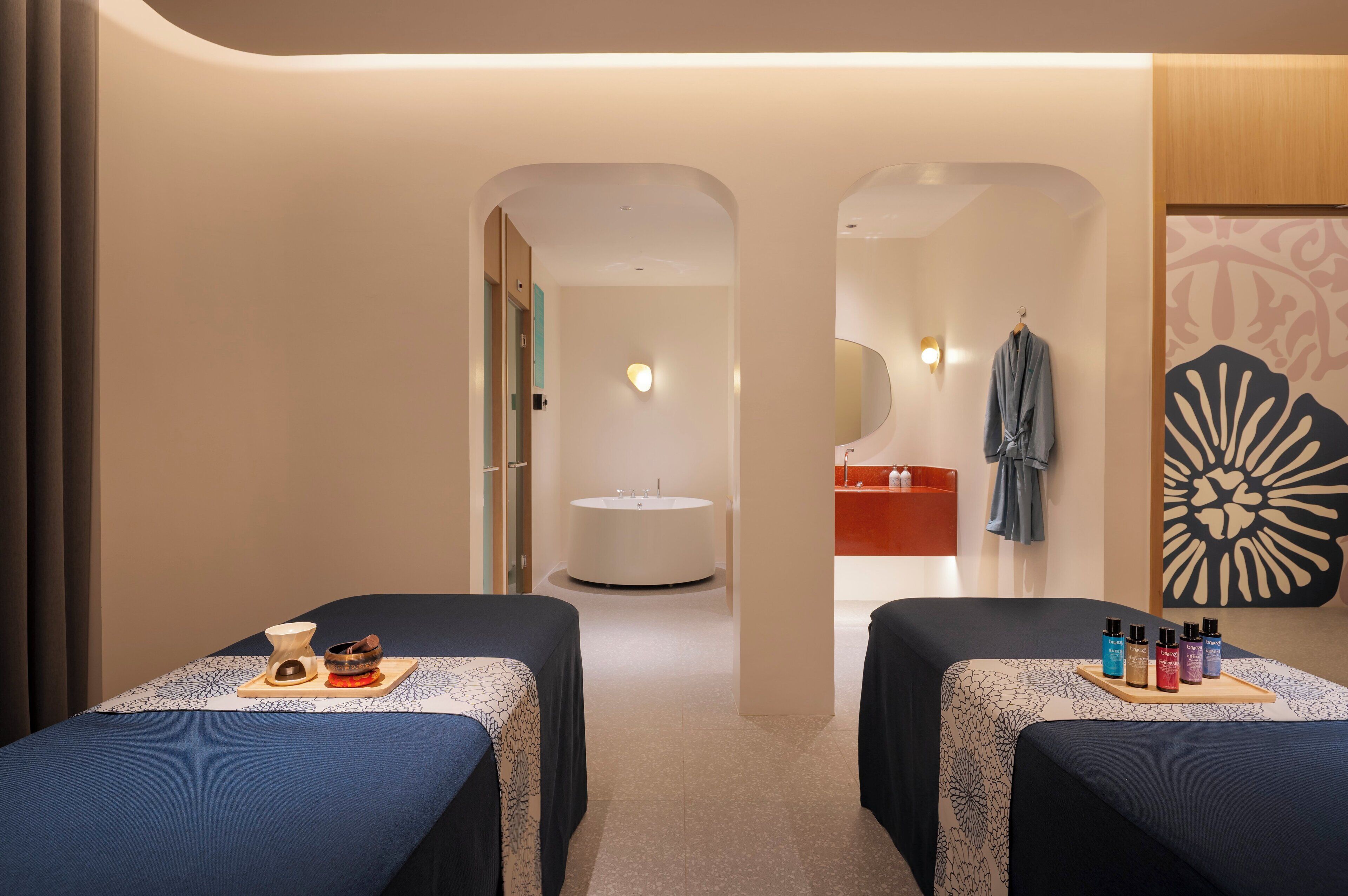 A spa room with two massage tables, a round sink, and a towel rack.