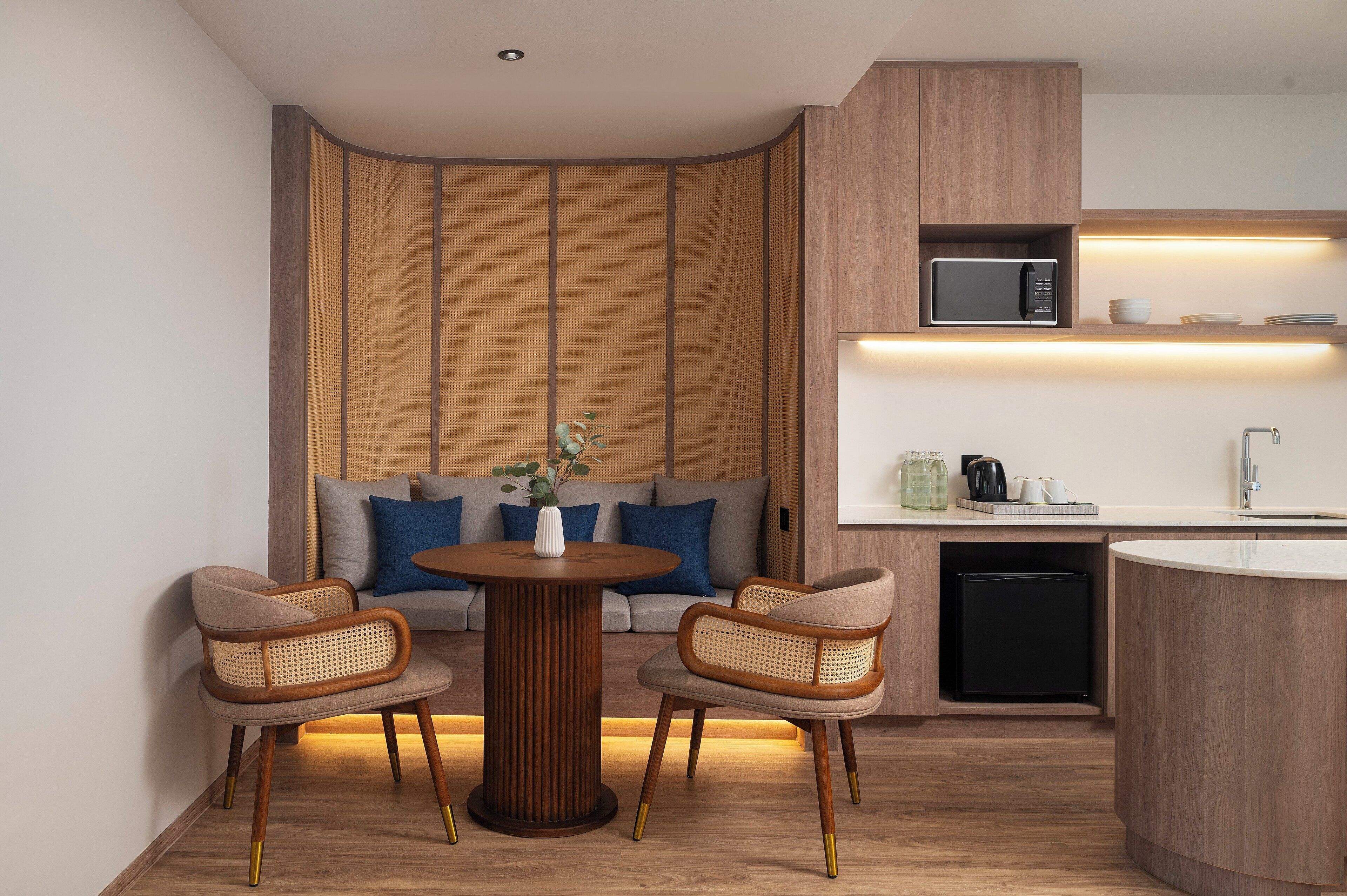 A modern kitchen with a microwave, sink, and a small refrigerator. There is a round table with two chairs and a sofa with cushions.