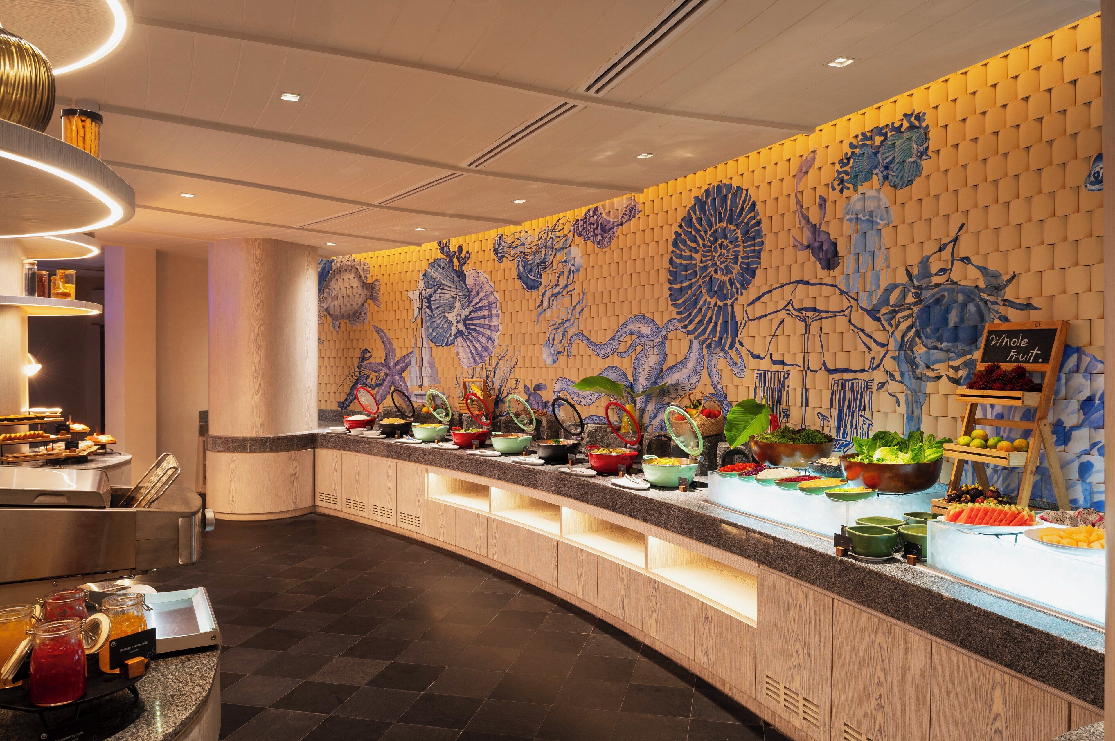 Un área de bufé con diversos alimentos y un mural decorativo en la pared.
