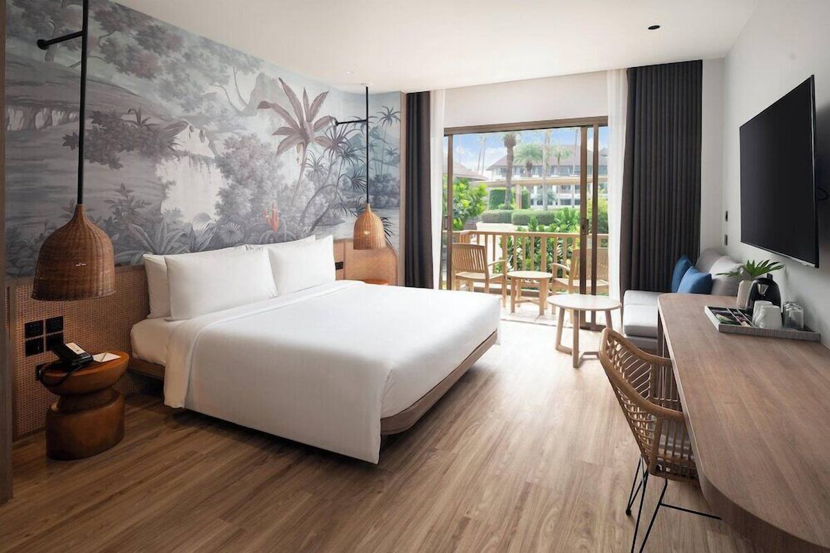 Una habitación de hotel moderna con una cama grande, zona de comedor, televisor y balcón con vistas.
