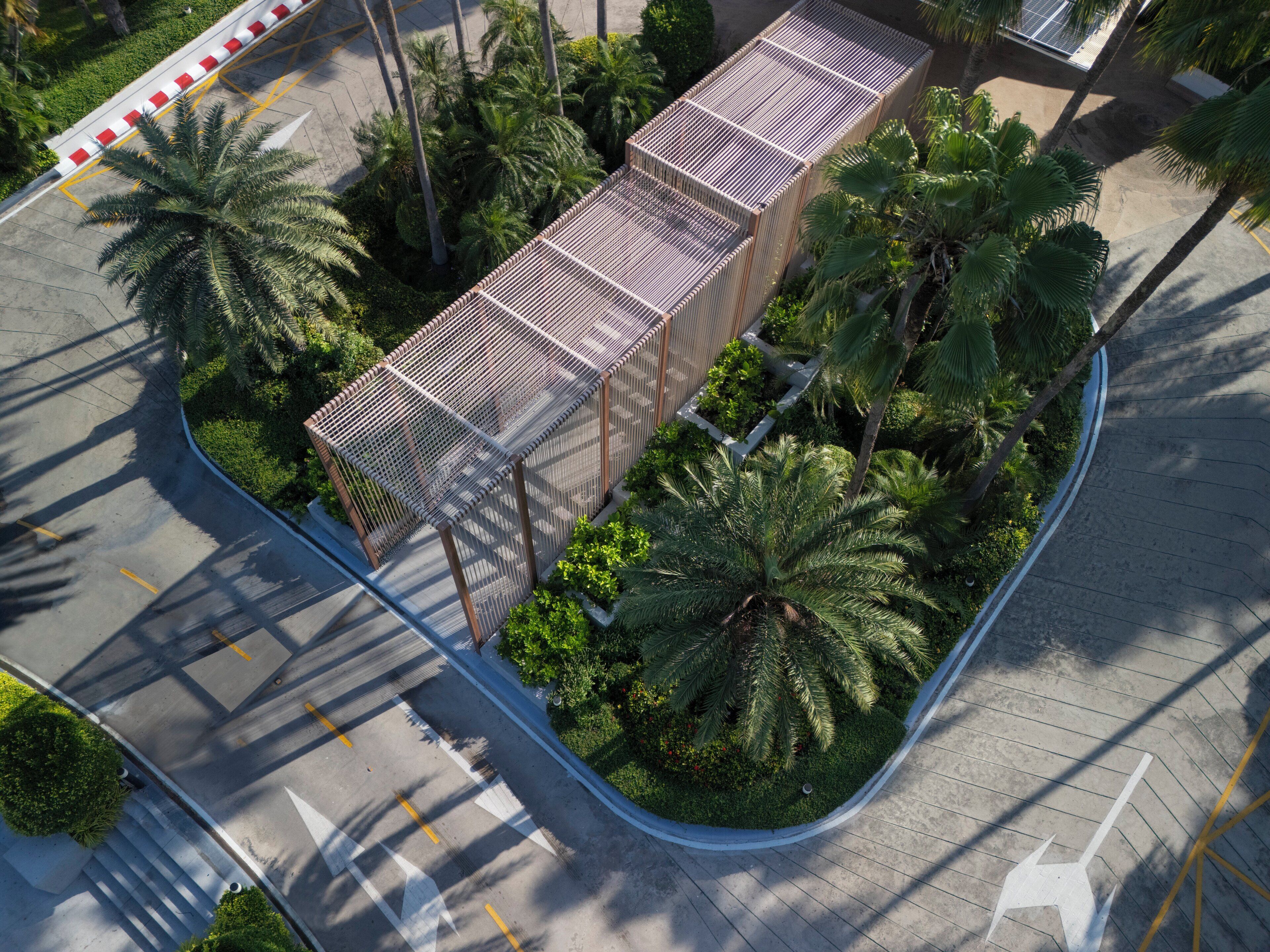 An aerial view of a modern building with a unique geometric design, surrounded by lush greenery and palm trees.