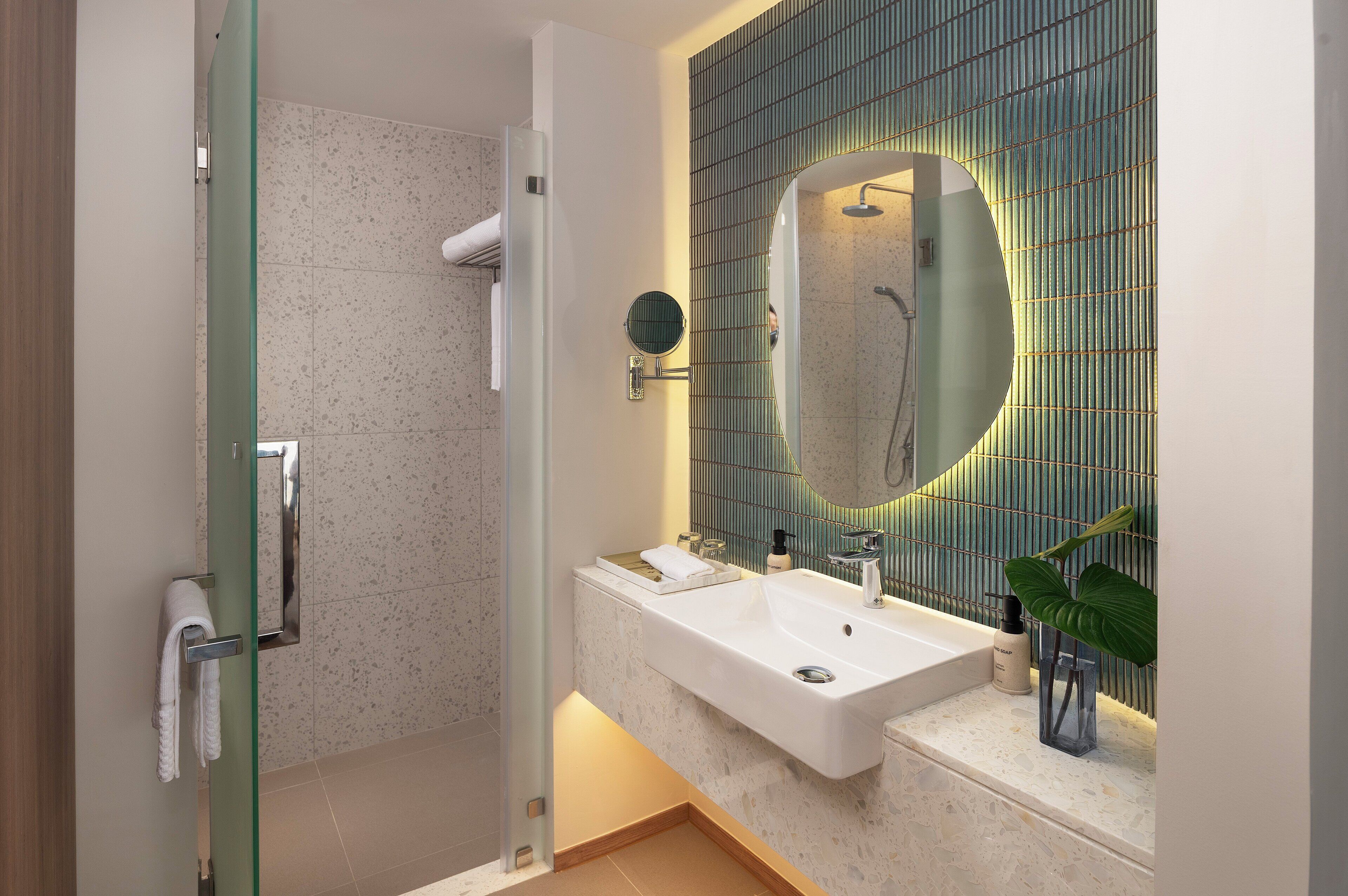 A modern bathroom with a glass shower enclosure, a large mirror, and a sink with a countertop.