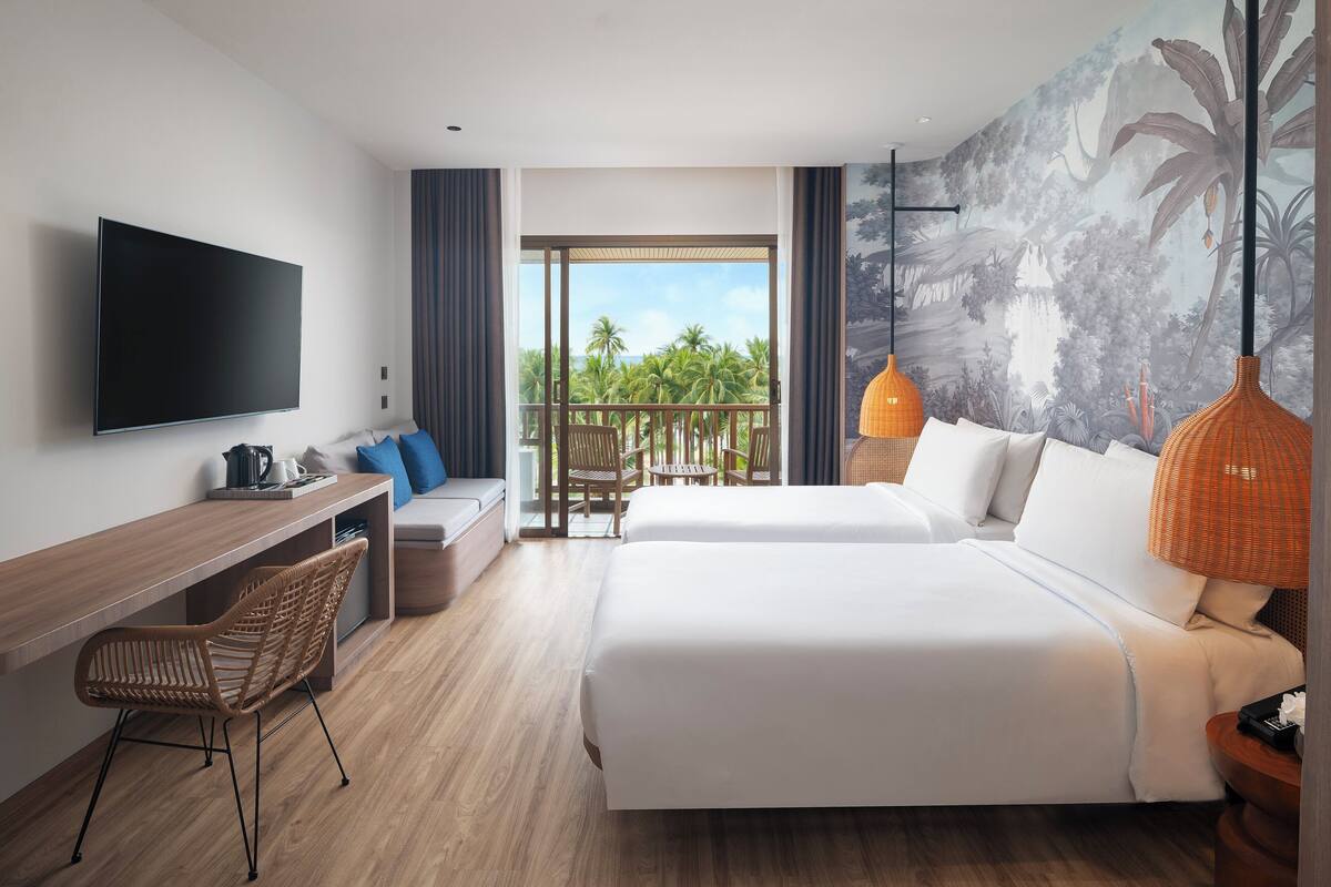 Habitación de hotel con una cama grande, un escritorio con silla, televisor de pantalla plana y balcón con vista a palmeras.