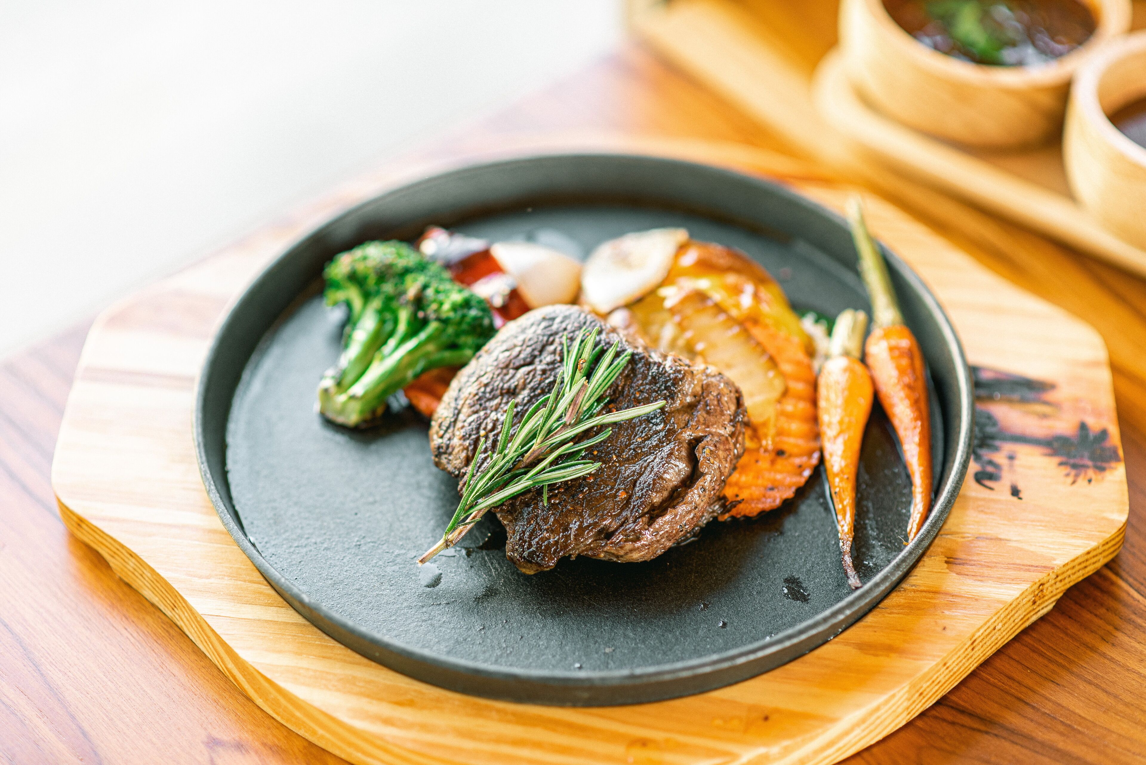 A plate of food with a steak, vegetables, and a garnish on a dark plate.