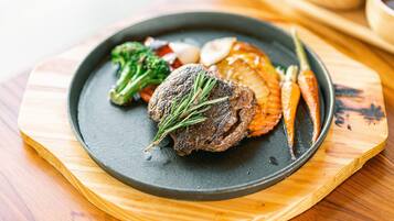 A plate of food with a steak, vegetables, and a garnish on a dark plate.