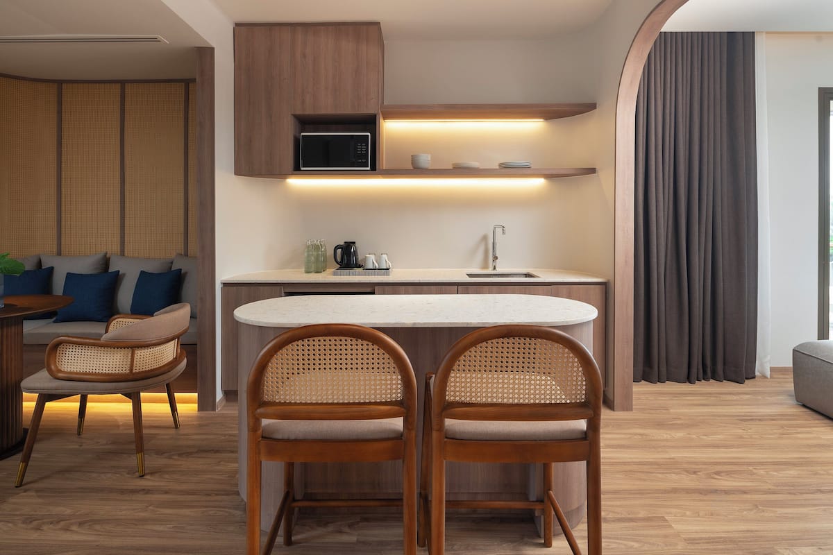 Cocina moderna con microondas, lavaplatos y taburetes de bar. Hay una zona de comedor con sofá y sillas.