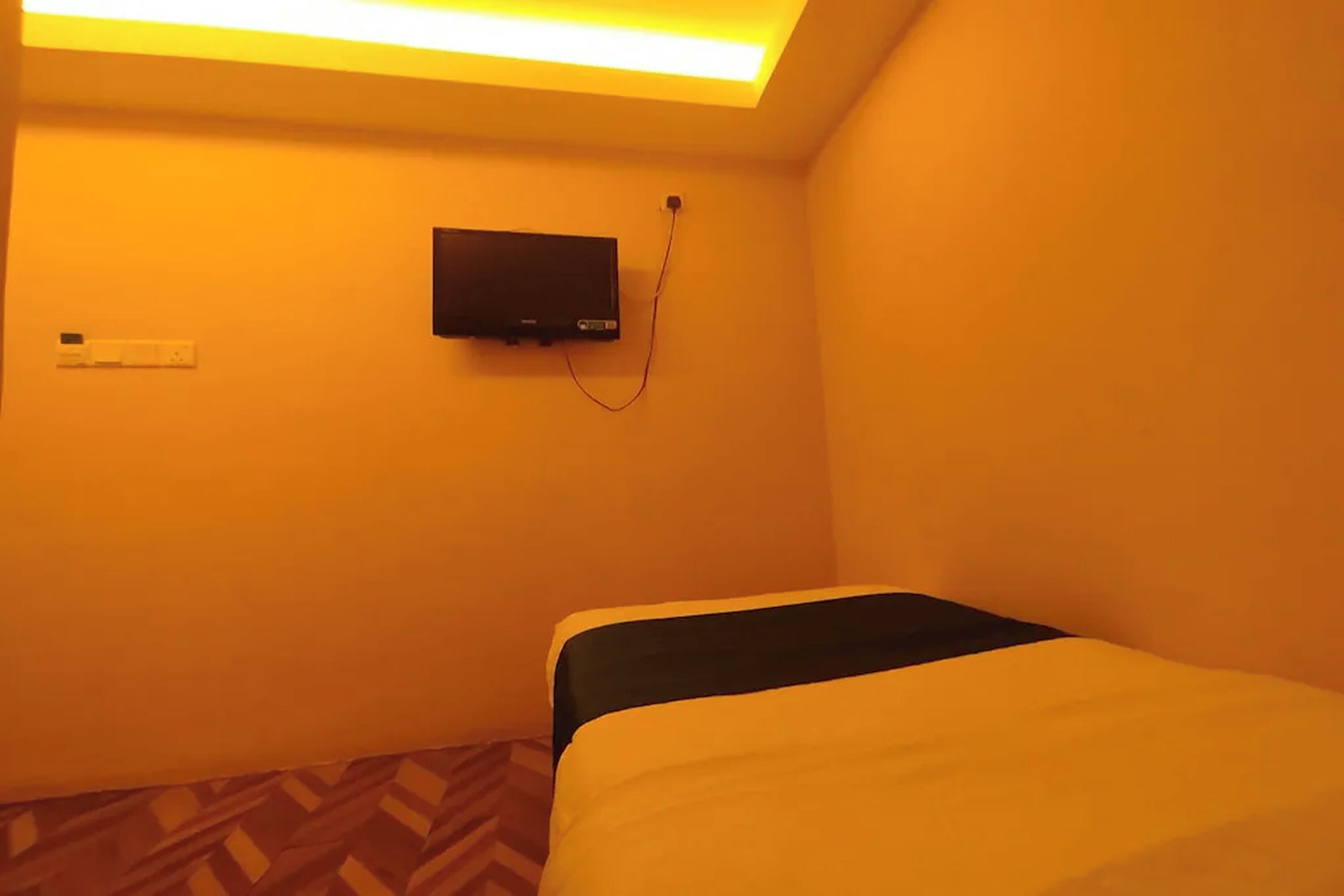 Una habitación pequeña con una cama, un televisor en la pared y una alfombra estampada.