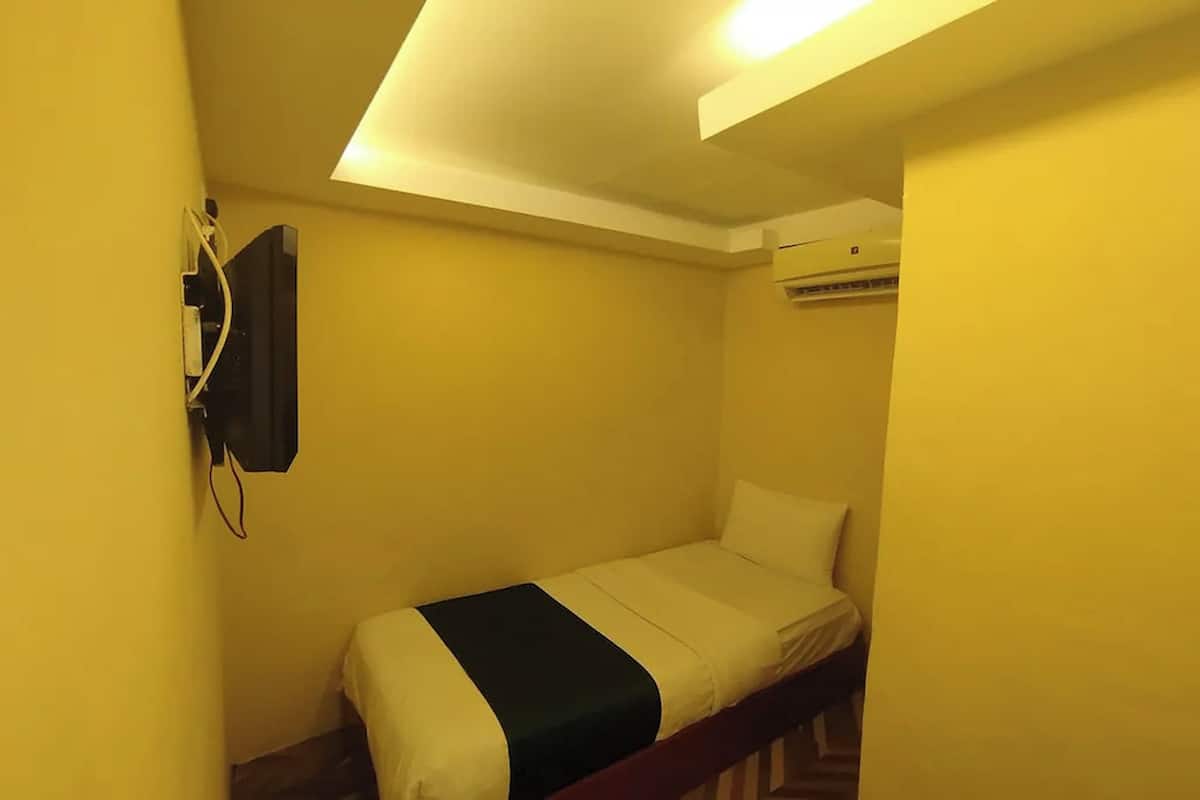 Una habitación pequeña con cama individual, televisión fijada a la pared y aire acondicionado.