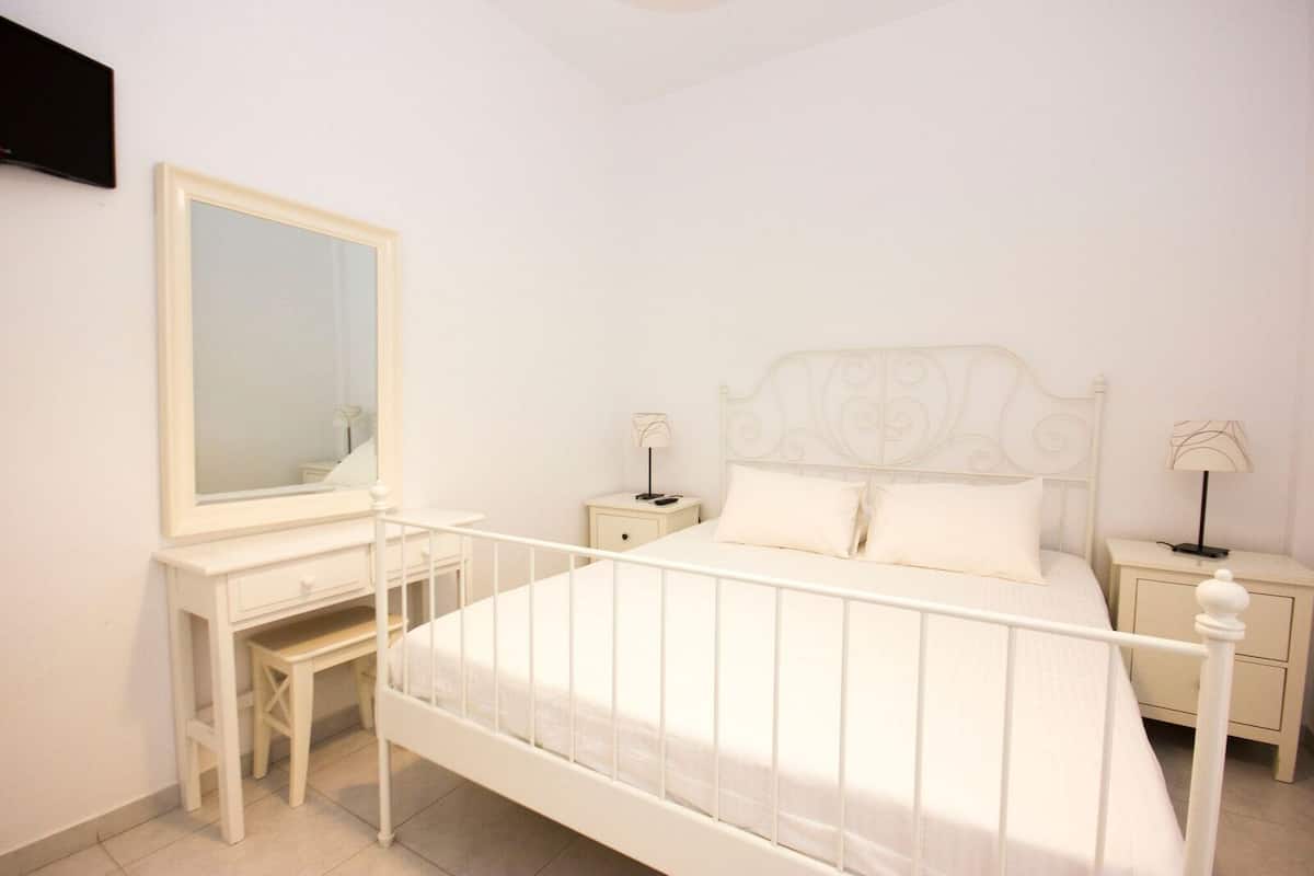 A white bedroom with a bed, a dresser, a mirror, and bedside tables with lamps.