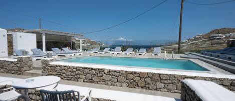 A pool area with lounge chairs and a table, surrounded by stone walls, overlooking a hilly landscape.
