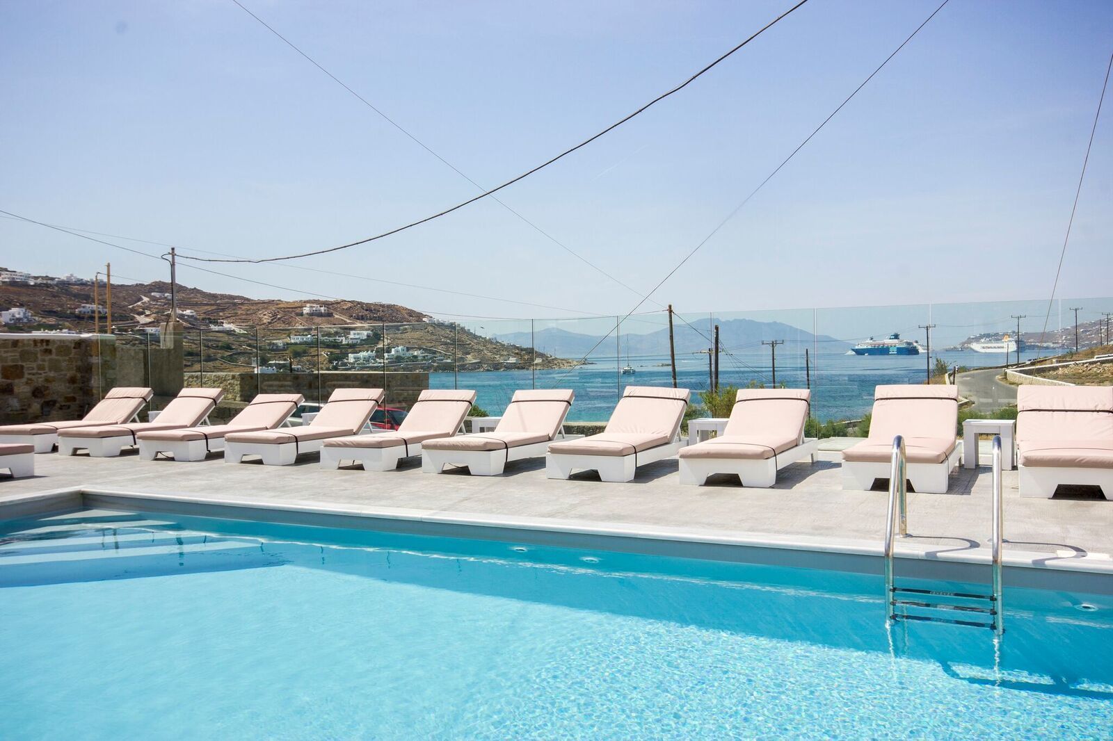 A poolside area with lounge chairs and a clear view of the sea and distant buildings.