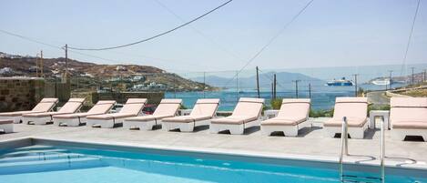 A poolside area with lounge chairs and a clear view of the sea and distant buildings.