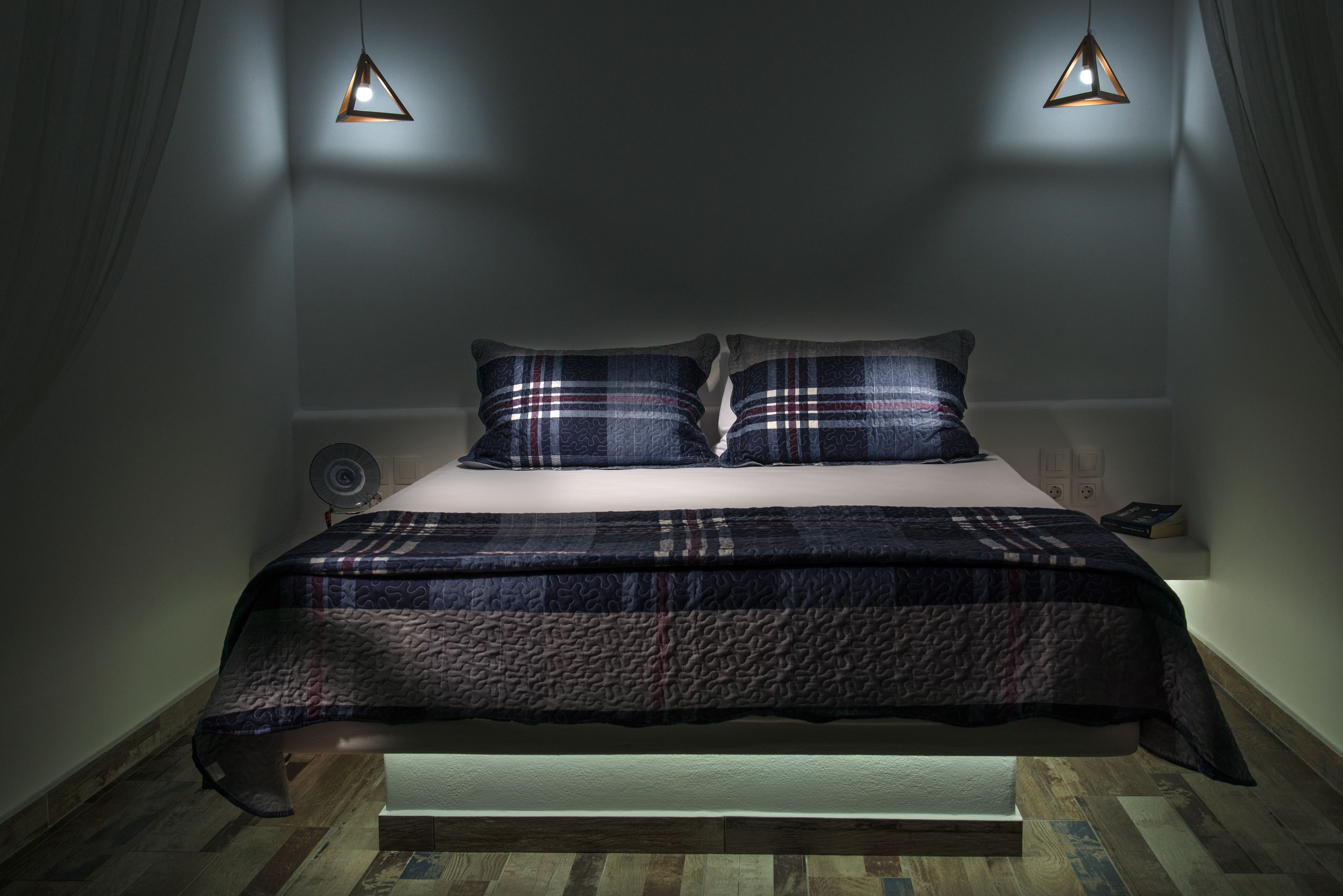 A bedroom with a bed, two pillows, a bedside table, and a lamp.