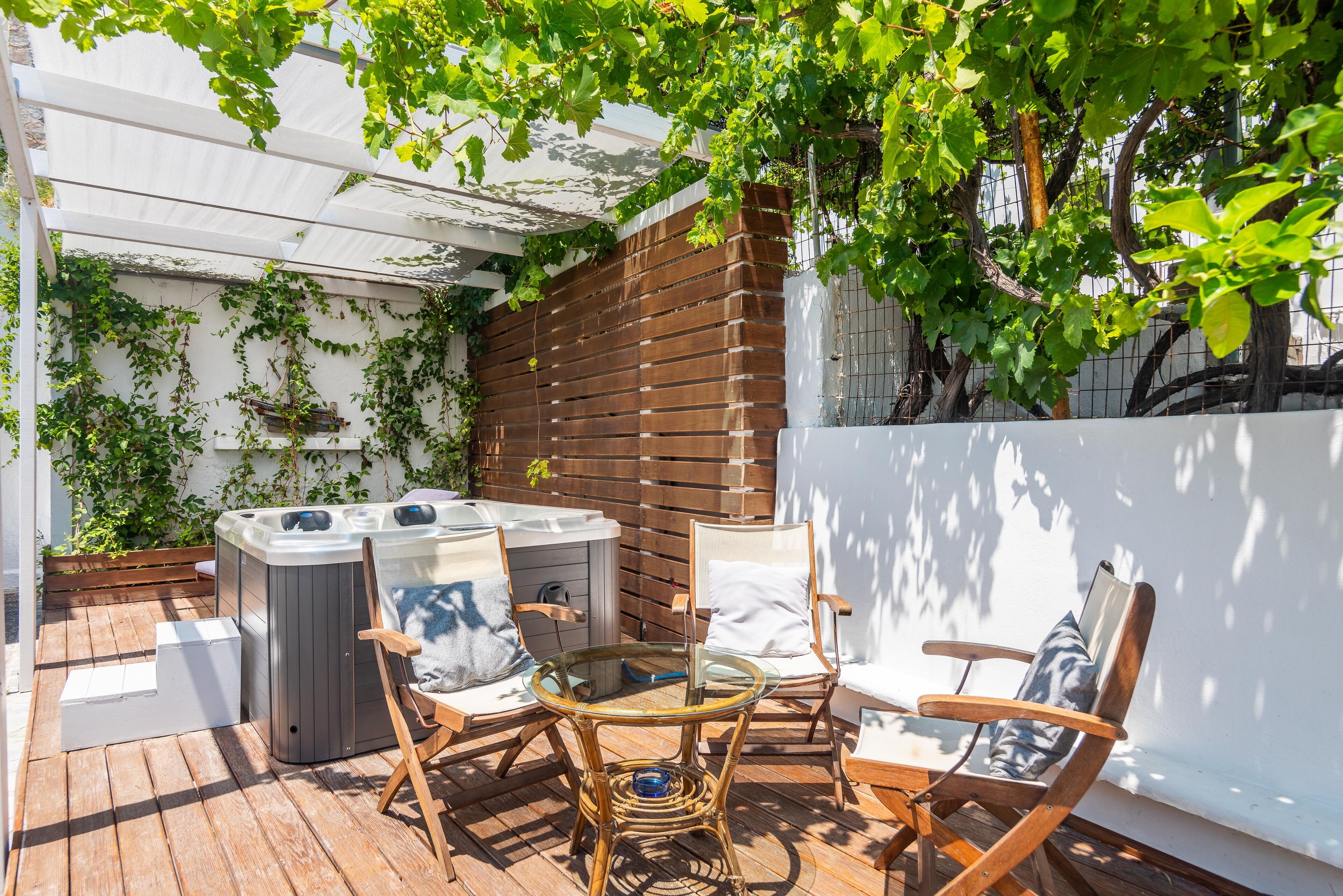 A patio with a hot tub, two wicker chairs, and a glass table.