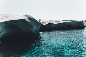A person jumping off a large rock into a body of water.