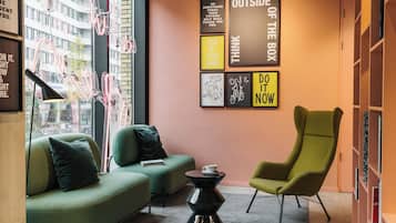 A modern lounge area with a green sofa, a green armchair, and a black coffee table. There are motivational posters on the wall and a window with a view of buildings.