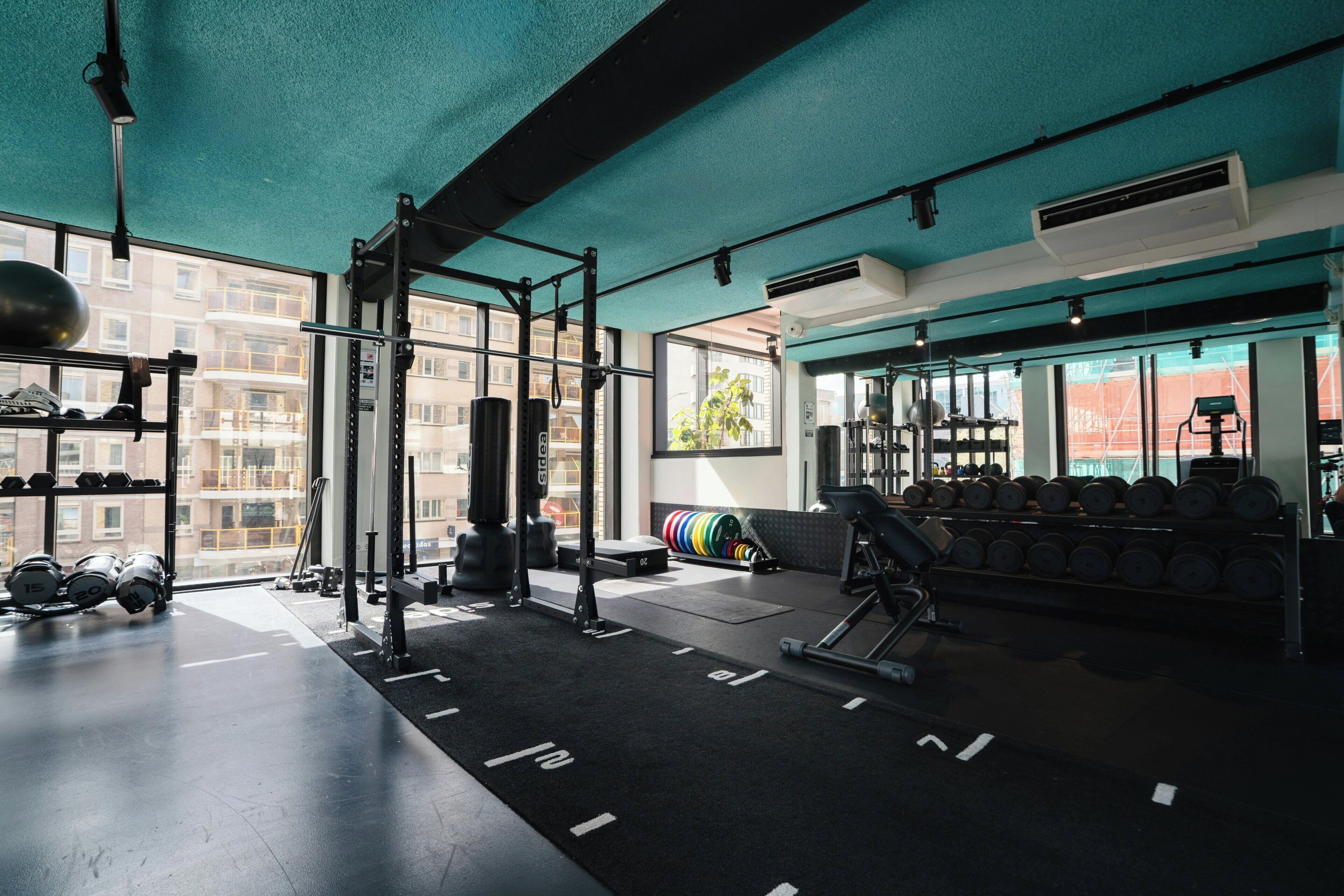 Un gimnasio con equipamiento de levantamiento de pesas, mancuernas y una jaula para sentadillas.
