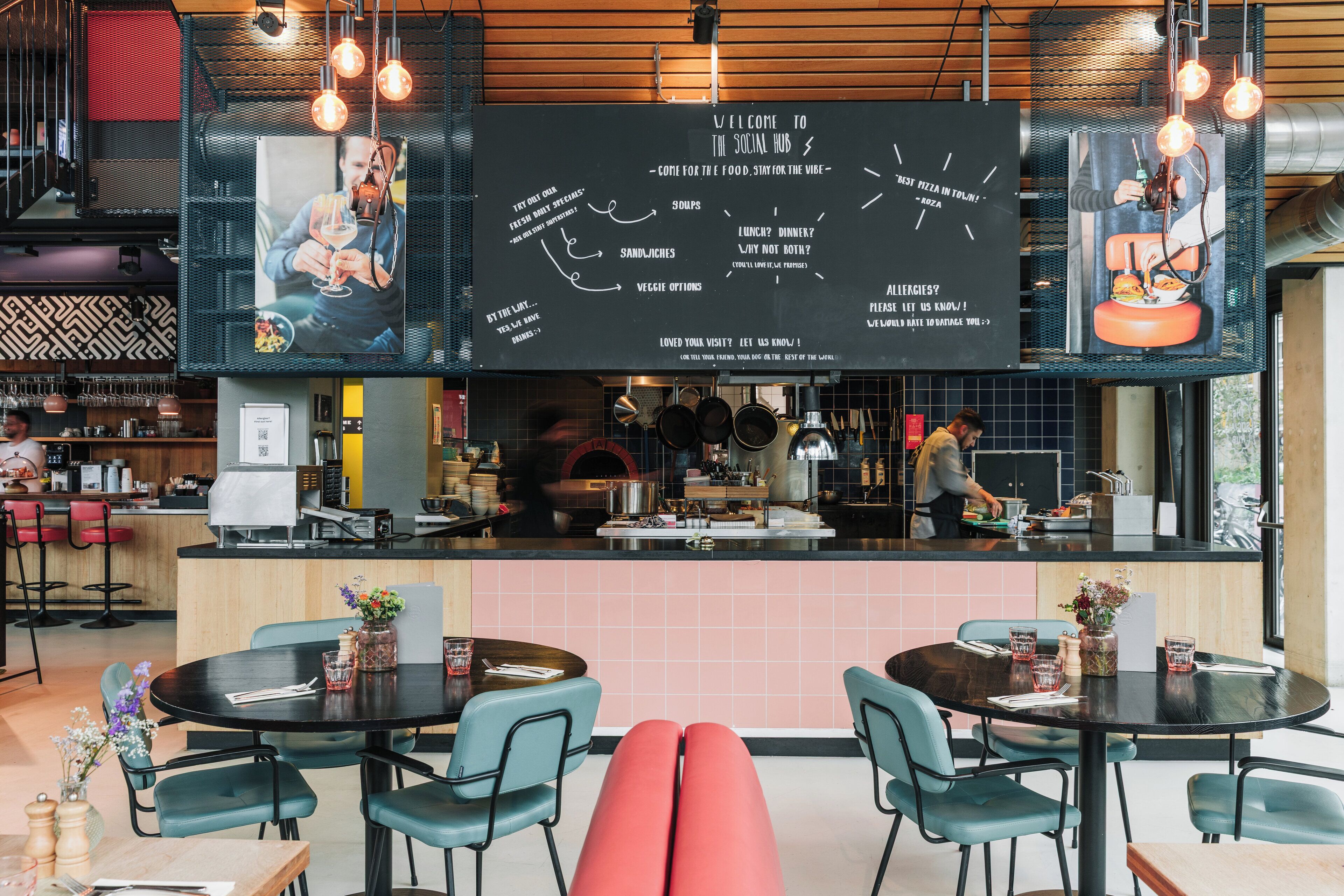 A modern restaurant interior with a central counter, round tables, and teal chairs.