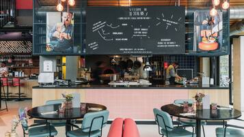 A modern restaurant interior with a central counter, round tables, and teal chairs.