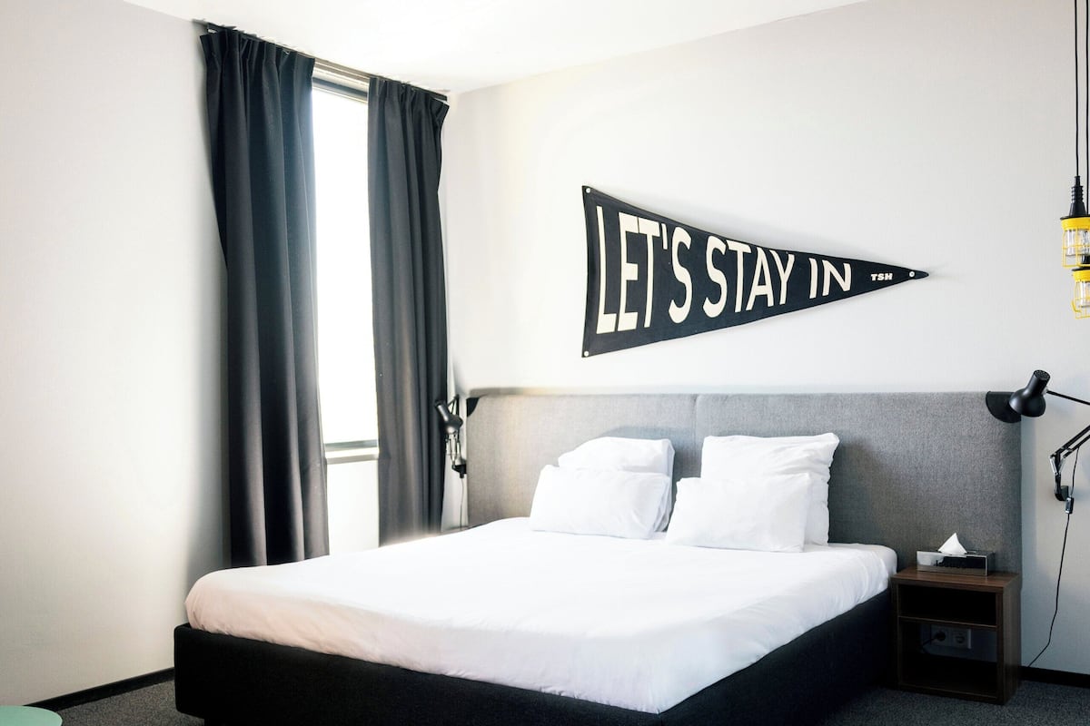 Ett modernt hotellrum med en stor säng, ett skrivbord, en stol och en skylt som är monterad på väggen.