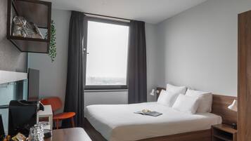 Habitación de hotel con cama, escritorio, silla, ventana con cortinas y una pequeña planta.