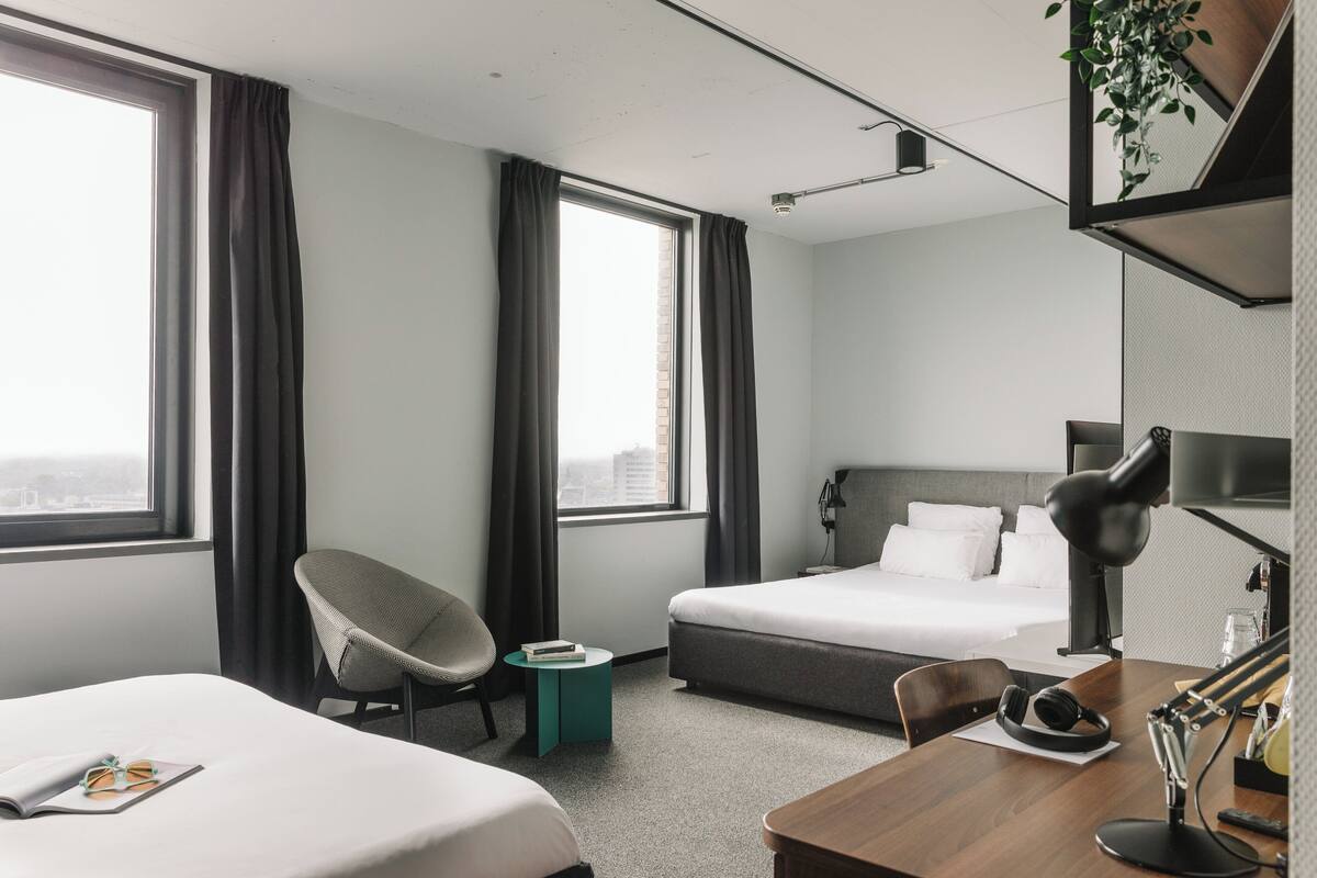 Ett hotellrum med två sängar, ett skrivbord, en stol, ett litet bord, en lampa och en växt.