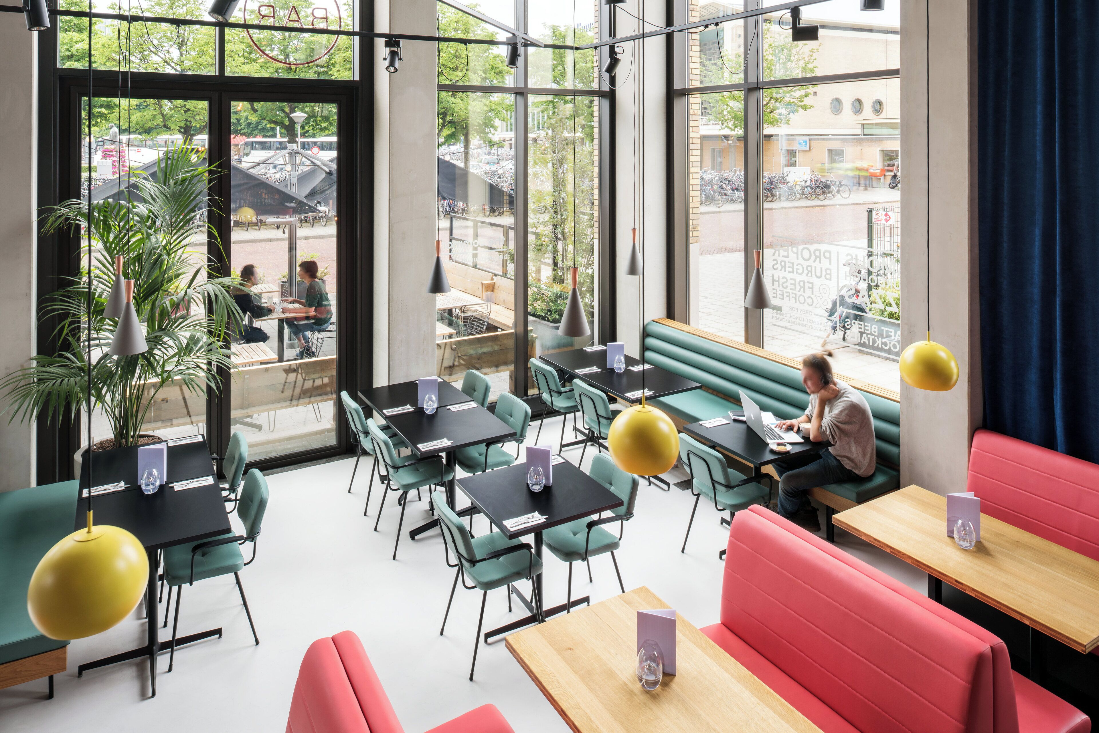 A modern cafe with green and red seating, large windows, and a view of the street.