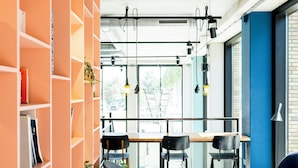 Un interior moderno con una estantería, una zona de comedor y un área de estar con un banco y un reposapiés.