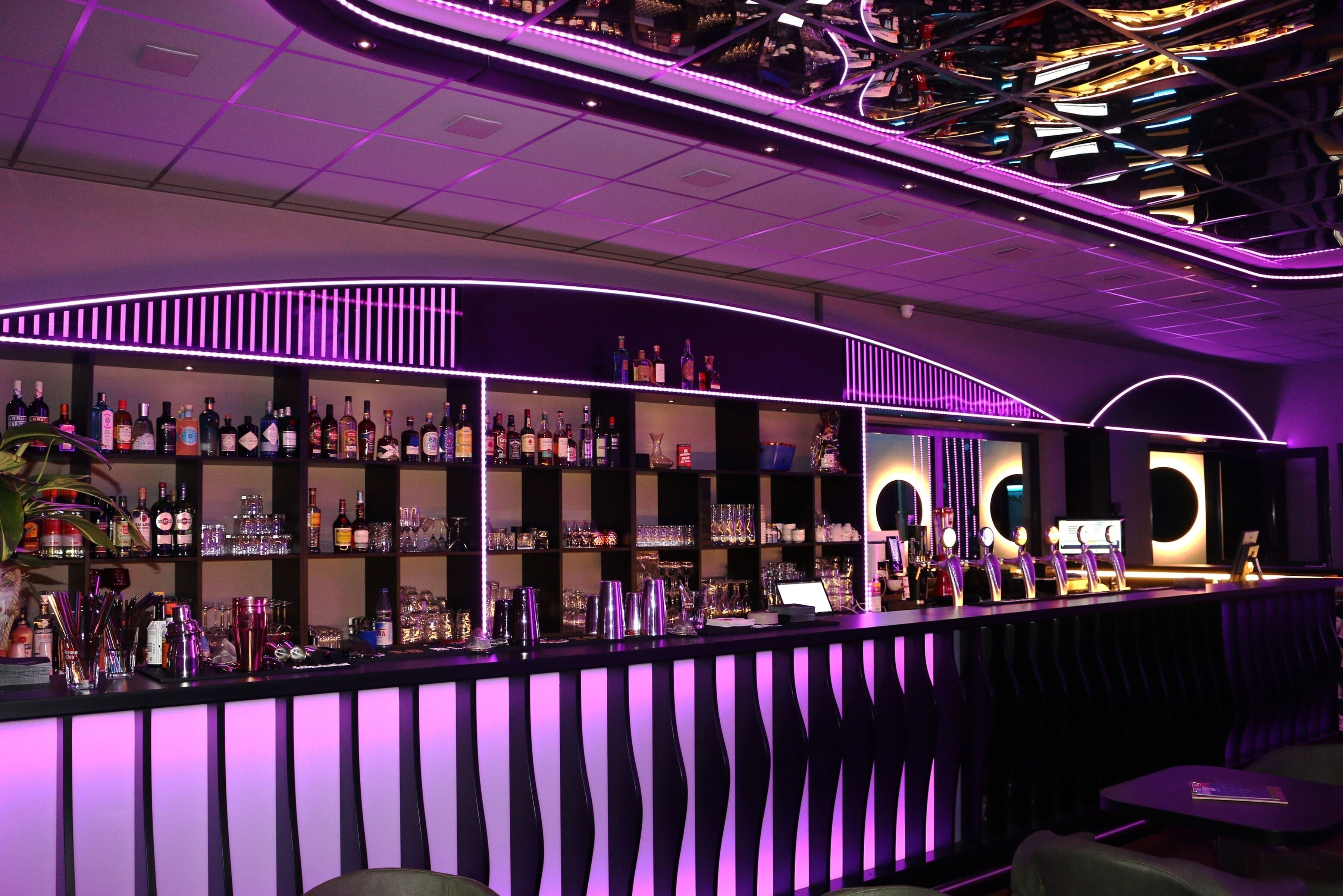 A bar area with shelves of bottles and glasses, a counter with a menu, and seating in the foreground.