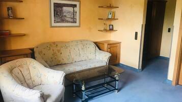 Una sala de estar con un sofá floral, una mesa de centro de vidrio y un cuadro en la pared.