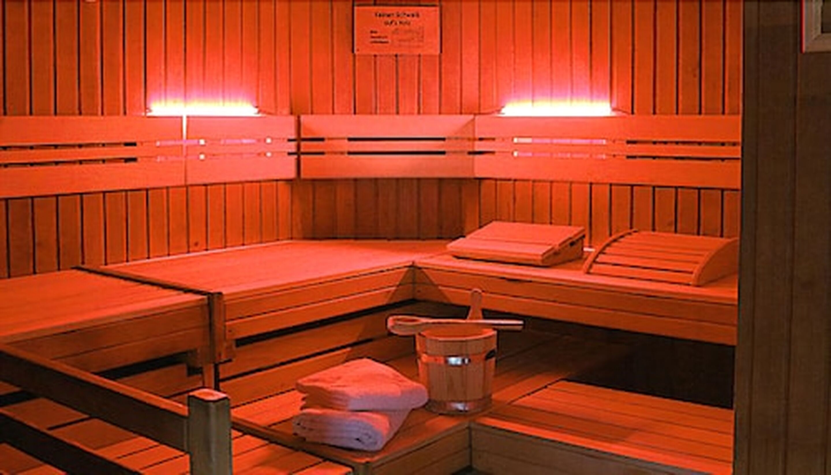 A sauna with wooden benches, towels, and a bucket.