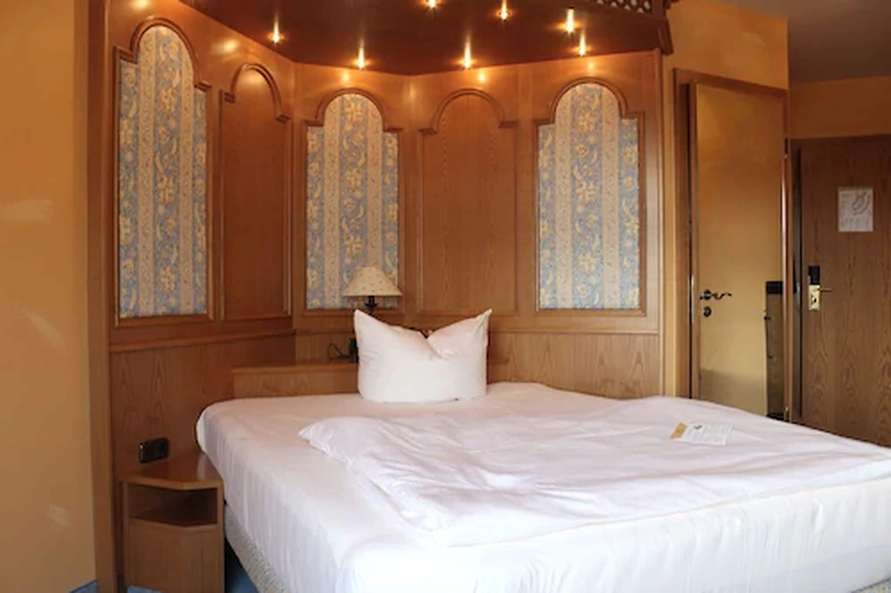 Ein Hotelzimmer mit einem großen Bett, Holzvertäfelung und einem dekorativen Fenster mit floralem Muster.