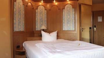 Ein Hotelzimmer mit einem großen Bett, Holzvertäfelung und einem dekorativen Fenster mit floralem Muster.