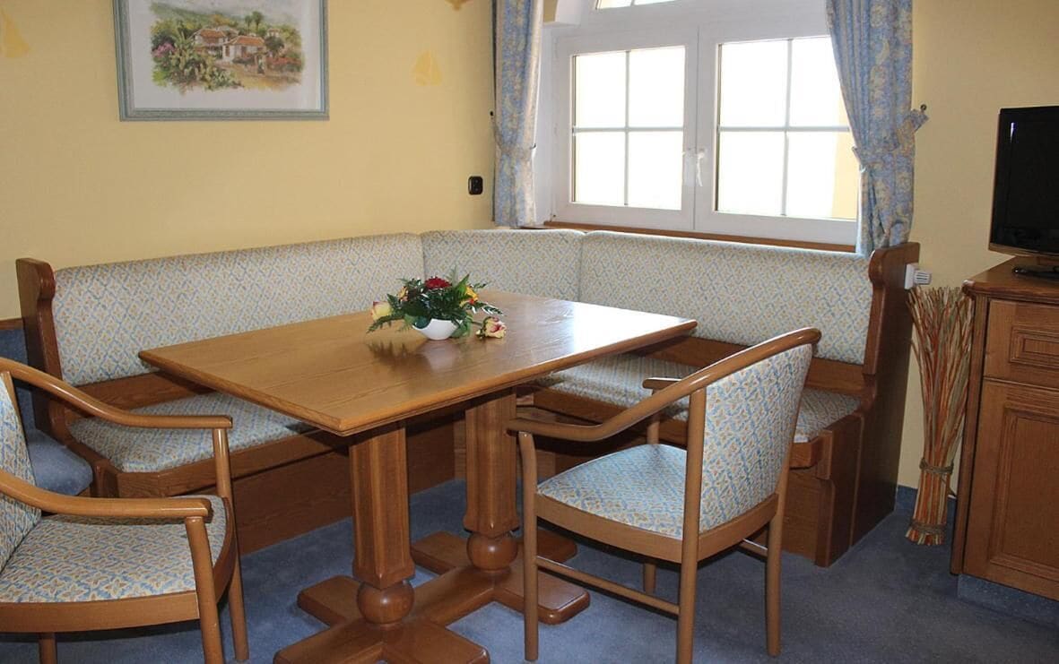 A dining area with a wooden table and chairs, a flower vase, and a window with curtains.