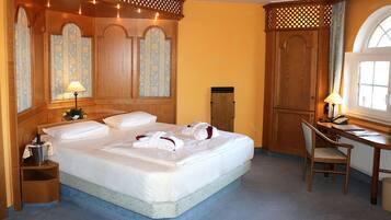 A hotel room with a large bed, wooden headboard, a desk with a chair, and a window with curtains.