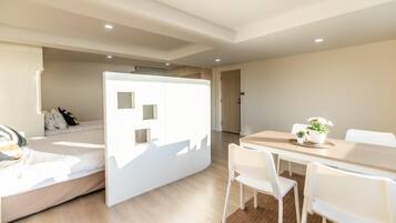 Een moderne hotelkamer met een bed, een witte scheidingswand met kleine ramen, een eettafel met stoelen en een kleine plant op de tafel.