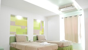 Une chambre d’hôtel avec deux lits, une fenêtre avec des rideaux, un appareil de climatisation et un mur décoré d’œuvres d’art abstraites.