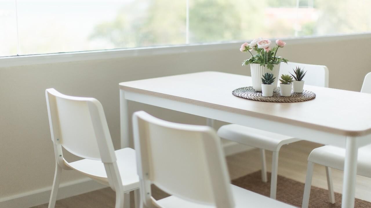 A white dining table with four chairs, a woven placemat, and small potted plants.
