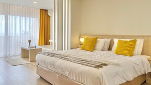 Une chambre d’hôtel moderne avec un grand lit, une table de chevet, une lampe et une vue sur l’extérieur à travers des rideaux légers.