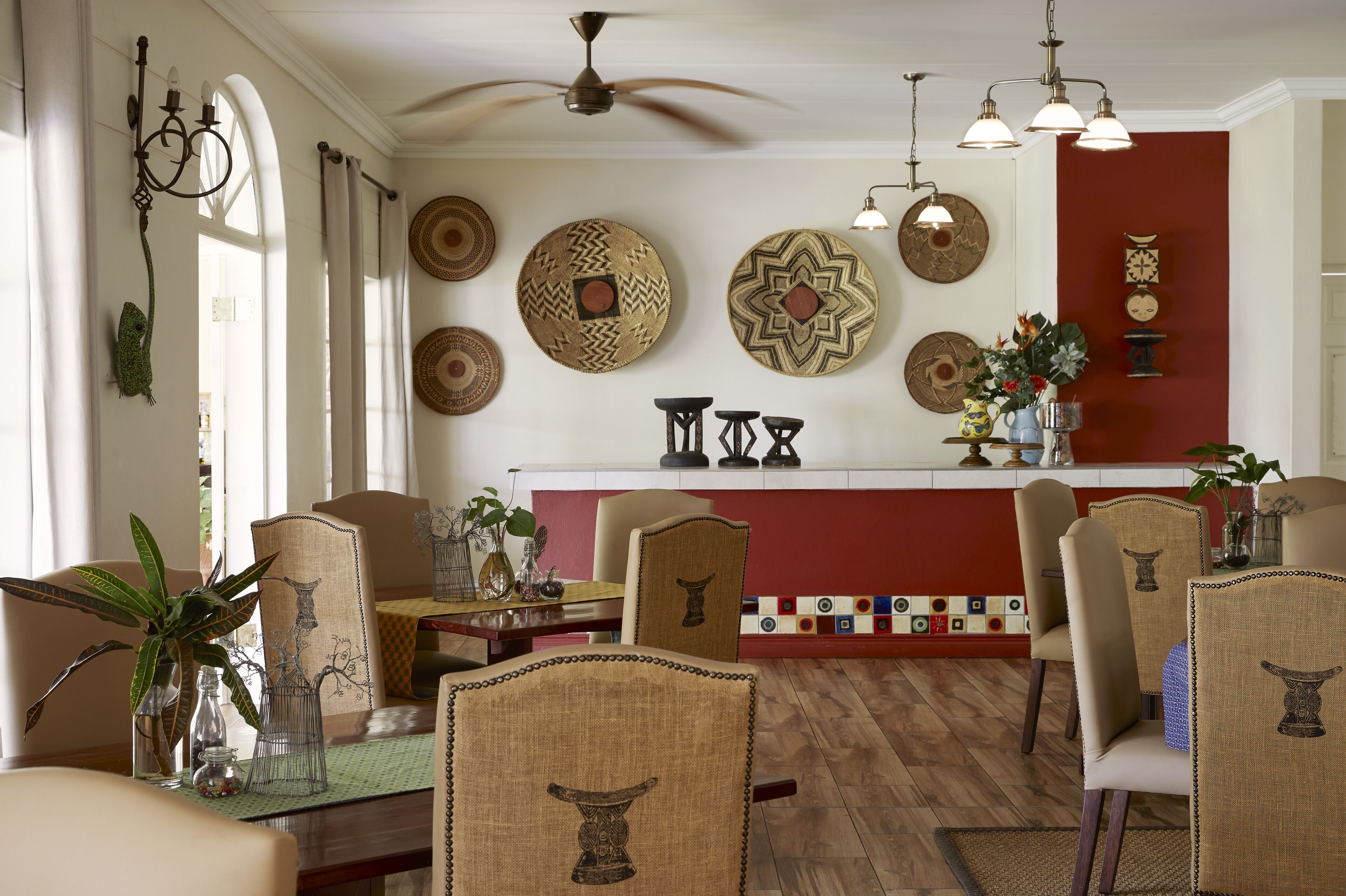 A dining area with a high ceiling fan, patterned wall decor, and a red accent wall.