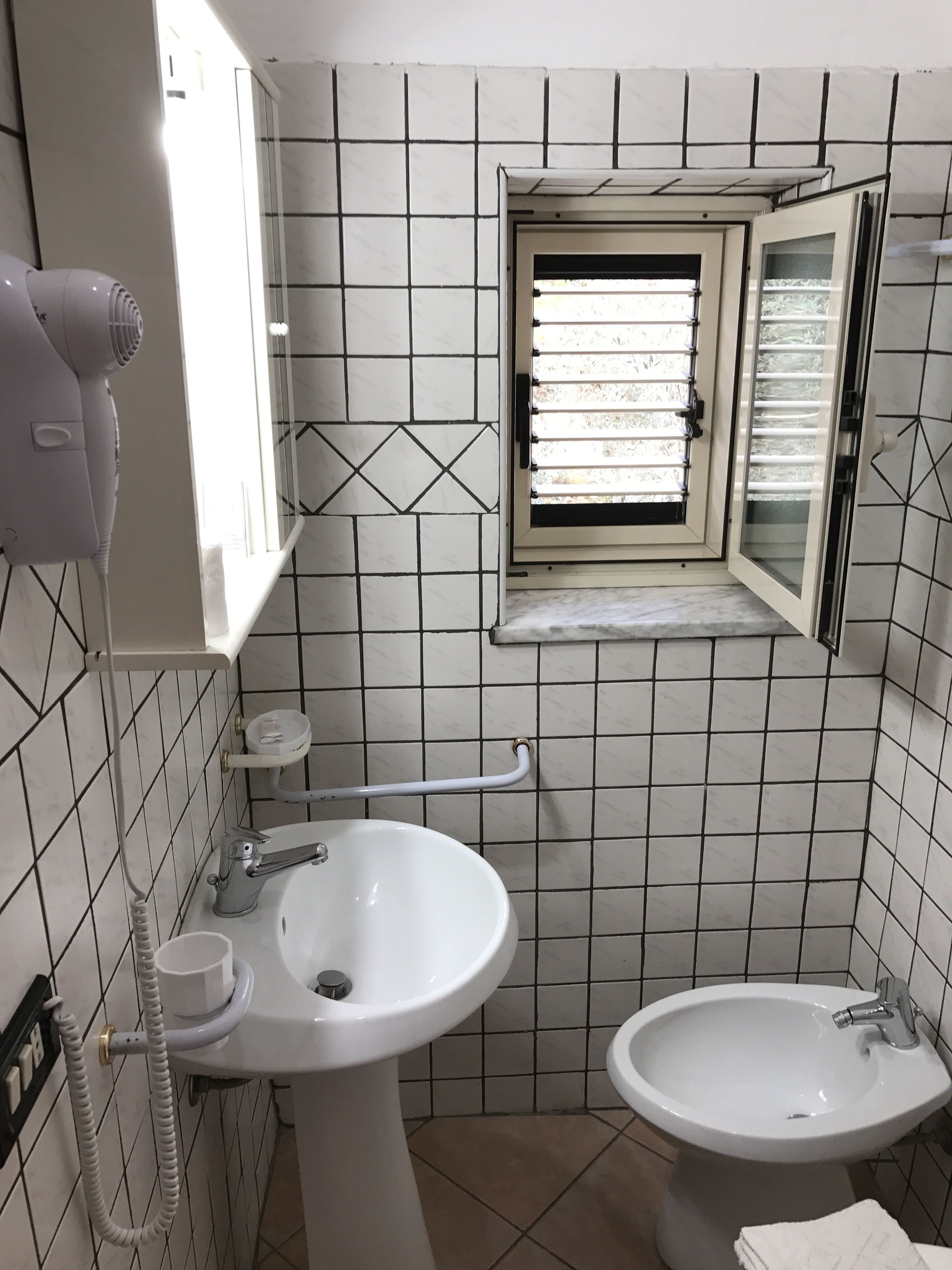 A bathroom with a sink, bidet, and a hairdryer on a wall-mounted shelf.