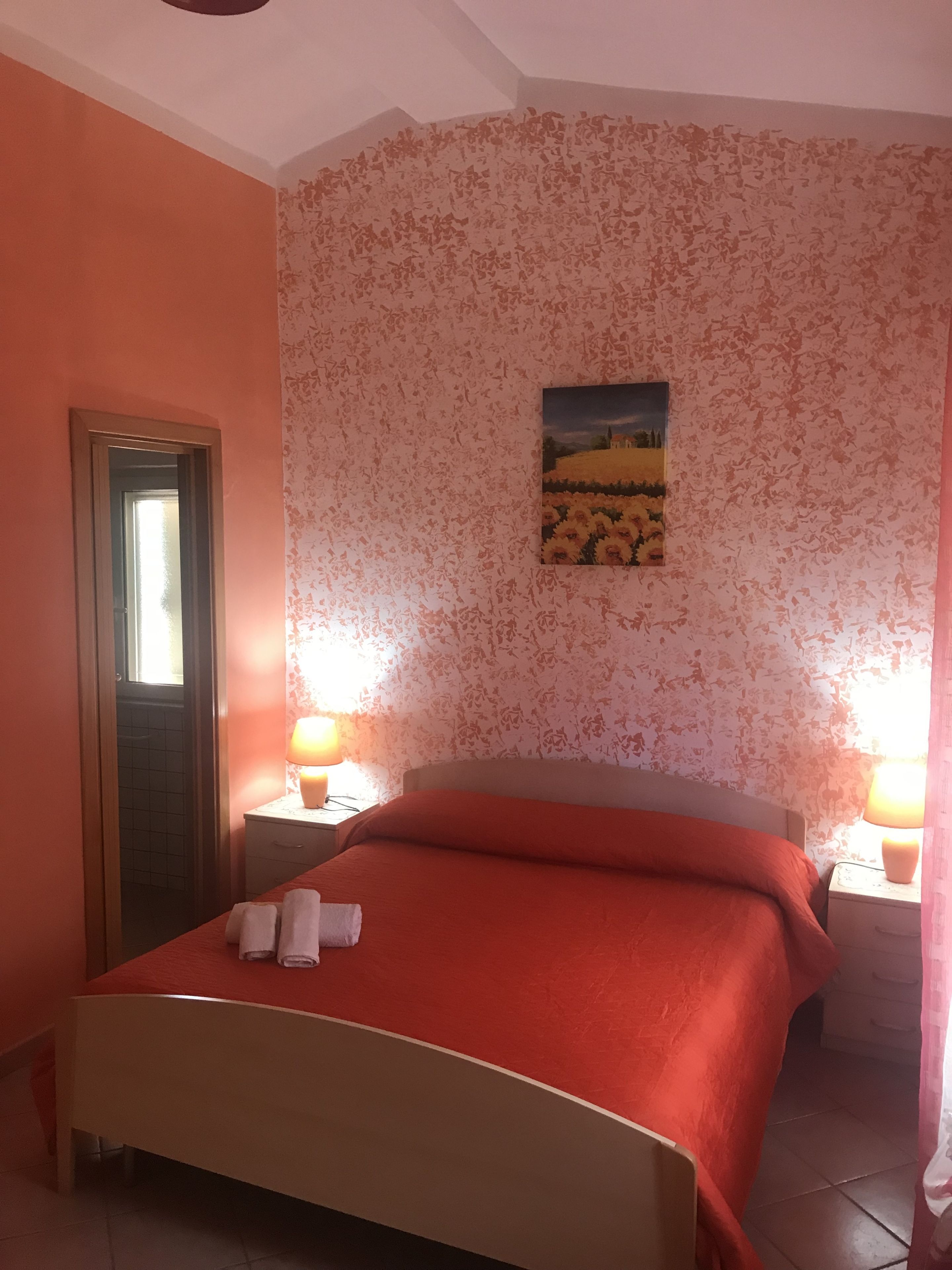 A bedroom with a bed, two bedside tables, a door, and a wall with a floral pattern.