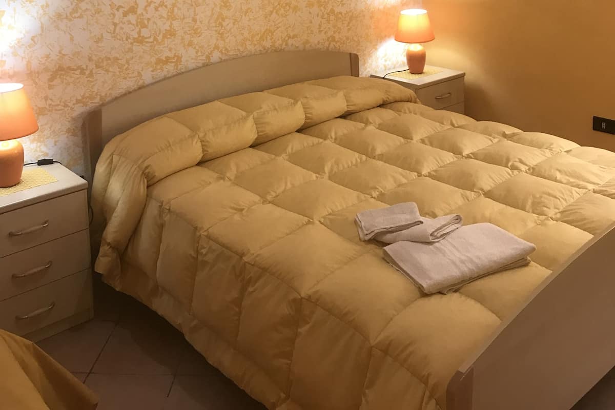 A bedroom with a bed, two bedside tables with lamps, a wall-mounted air conditioner, and a floral wallpaper.
