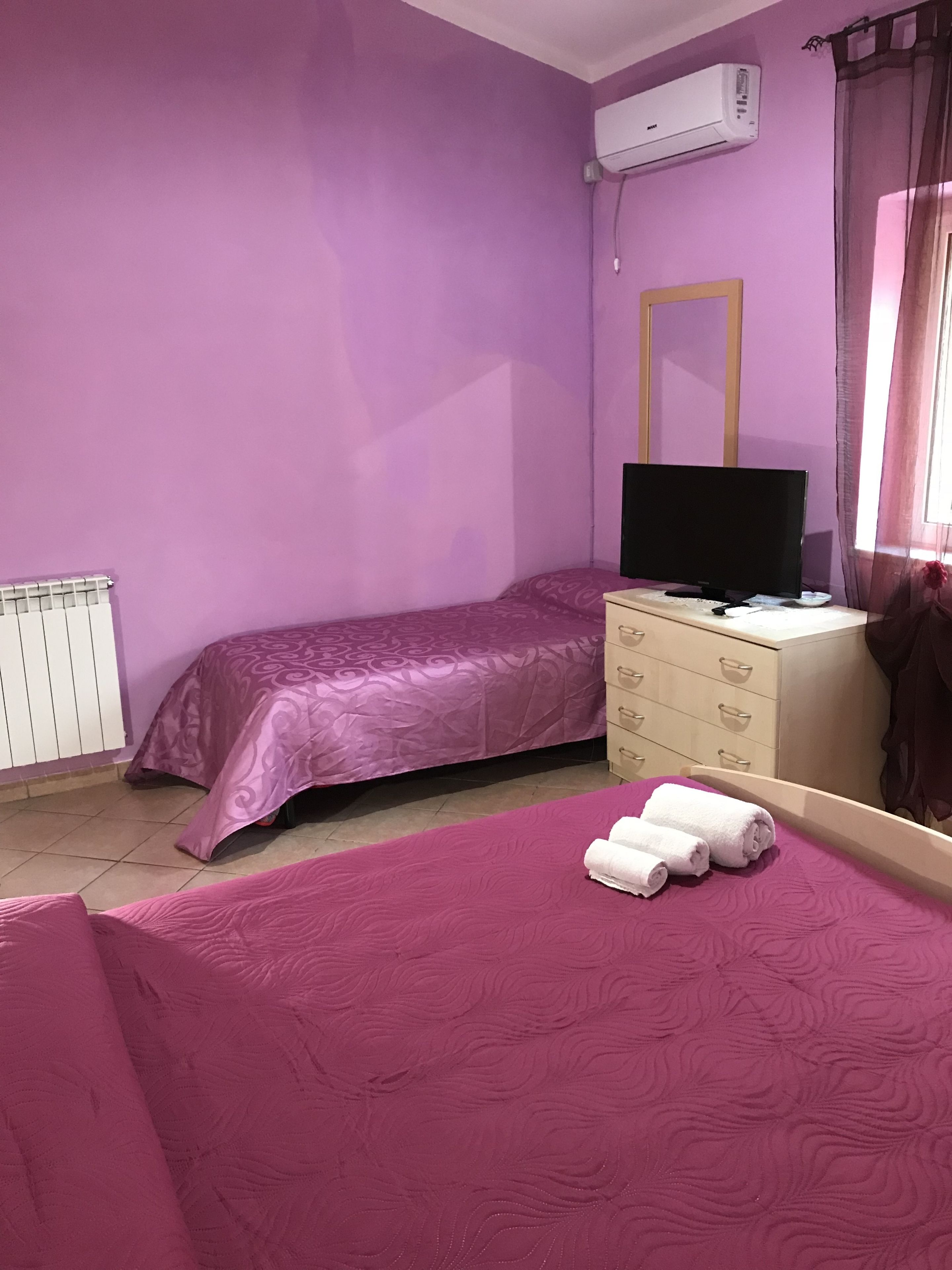 A room with purple walls, a bed with a matching purple bedspread, a dresser with a mirror, and a television on top.