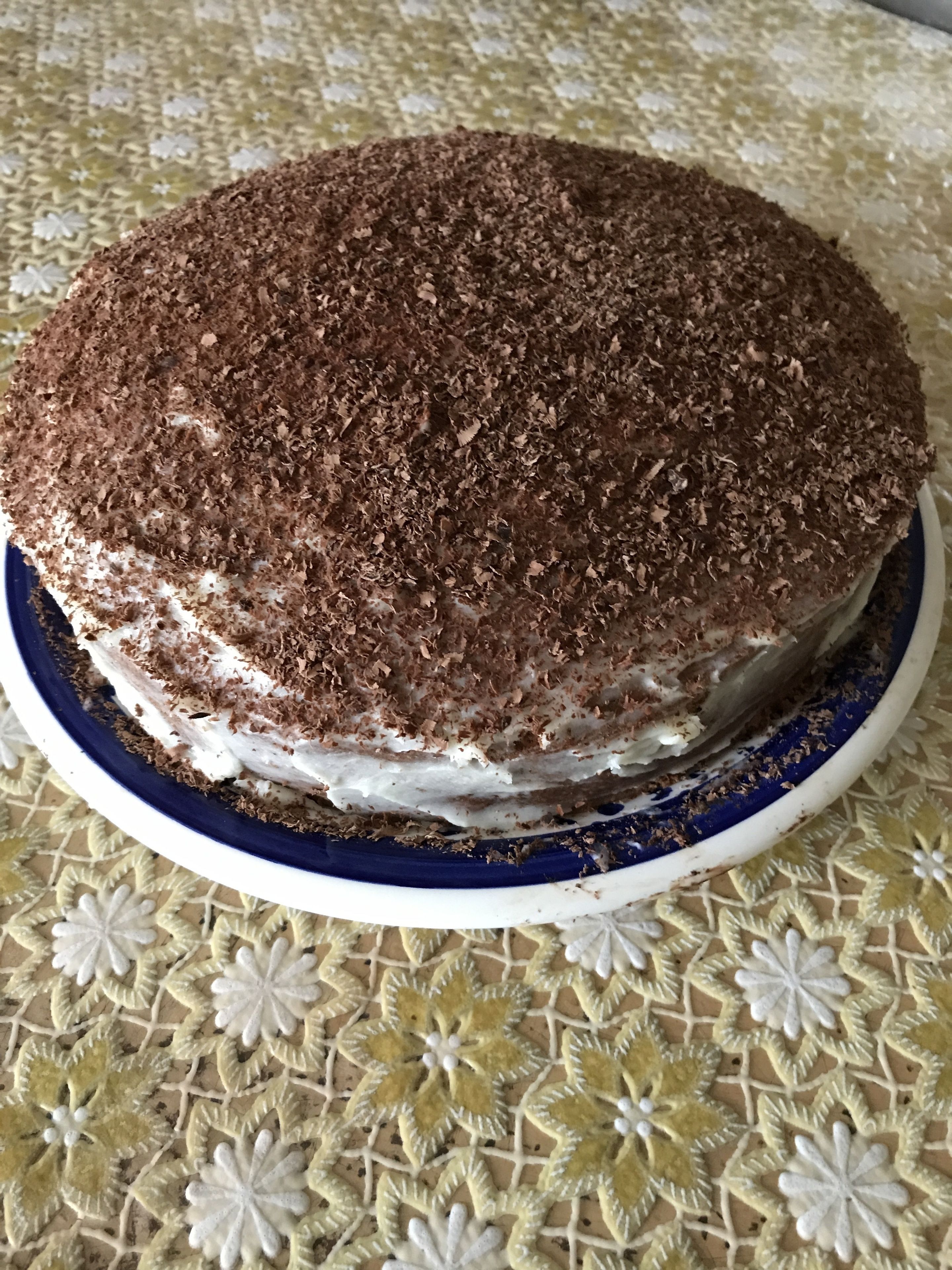 Postre redondo sobre un plato con borde azul, colocado sobre una mesa con mantel de flores.