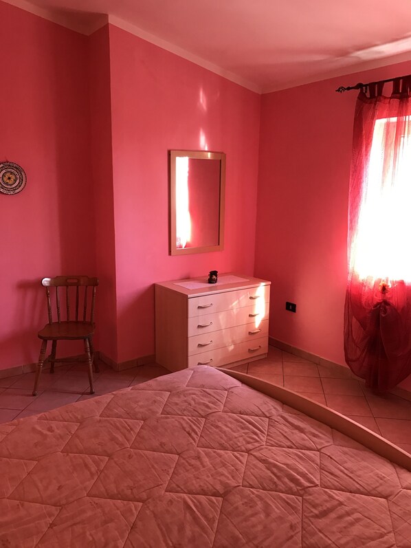 A bedroom with pink walls, a wooden chair, a dresser, and a bed with a quilted cover. - Bed & Breakfast Cilento (San Mauro Cilento)