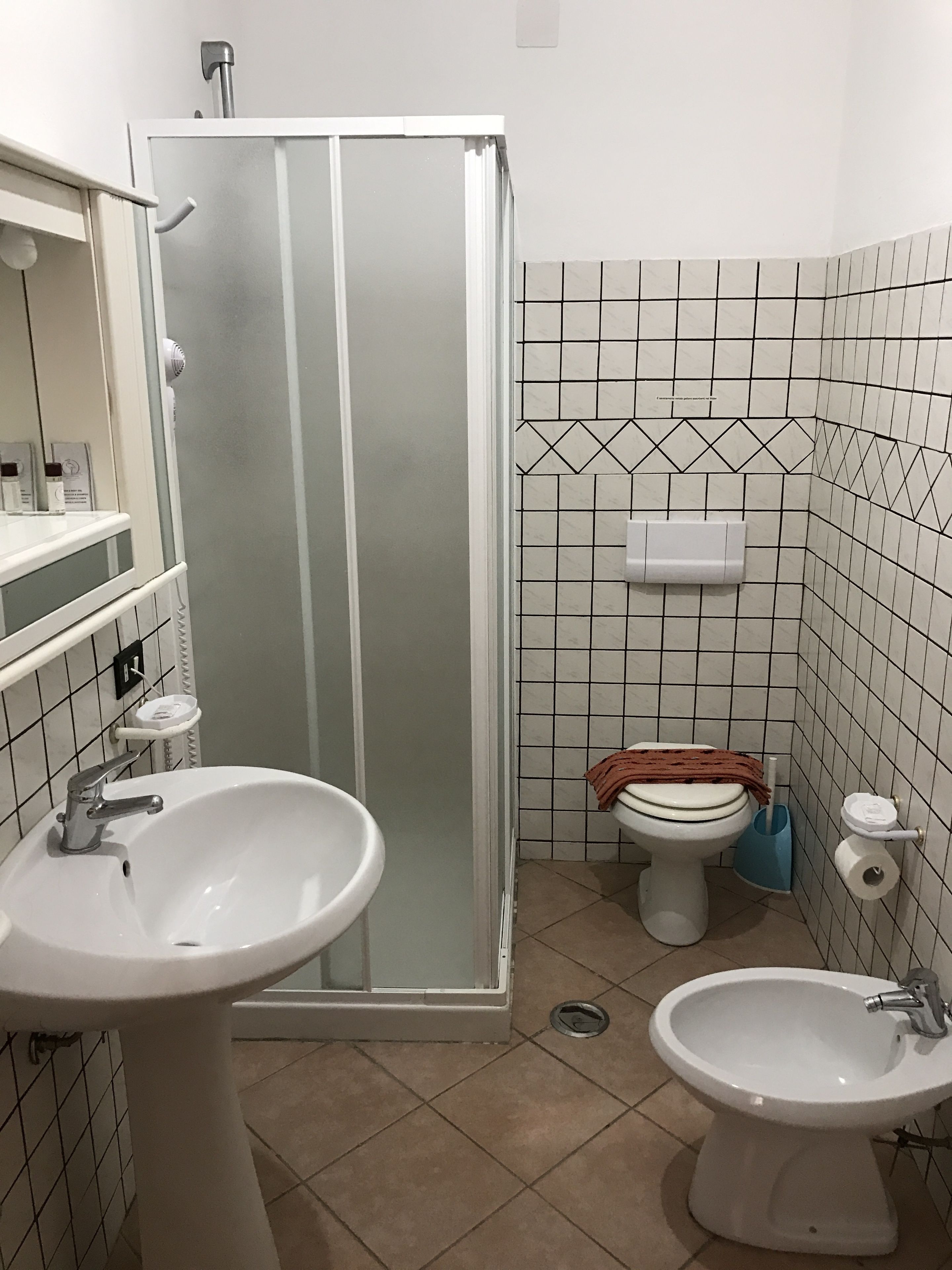 A bathroom with a shower enclosure, two sinks, a toilet, and a bidet.
