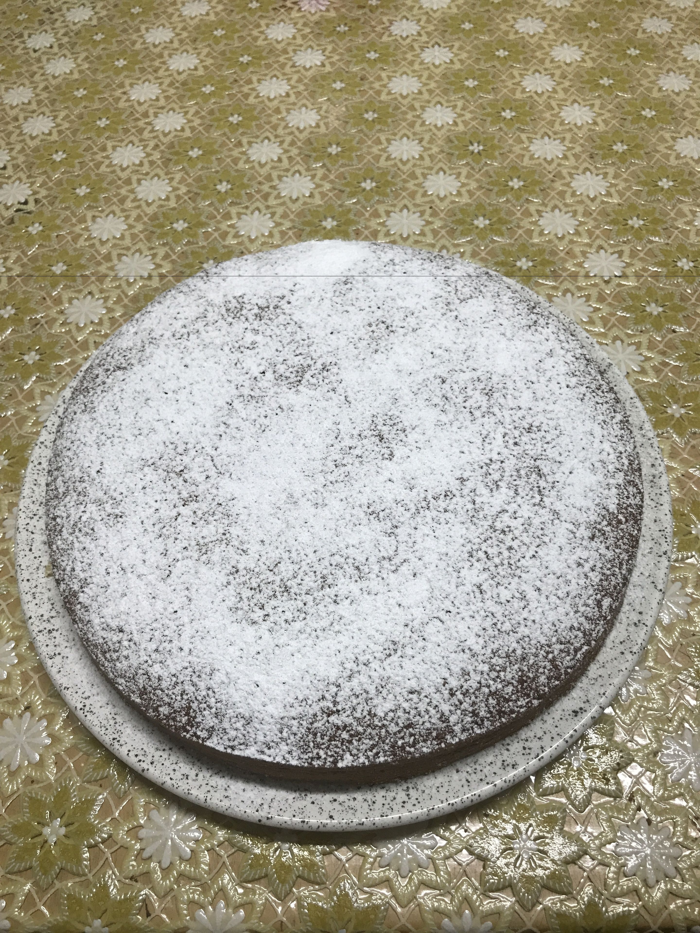 A round cake with powdered sugar on a decorative plate.