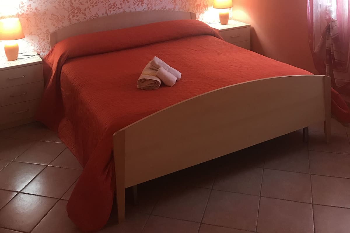 A bedroom with a bed, two bedside lamps, an air conditioner, and a floral wallpaper.
